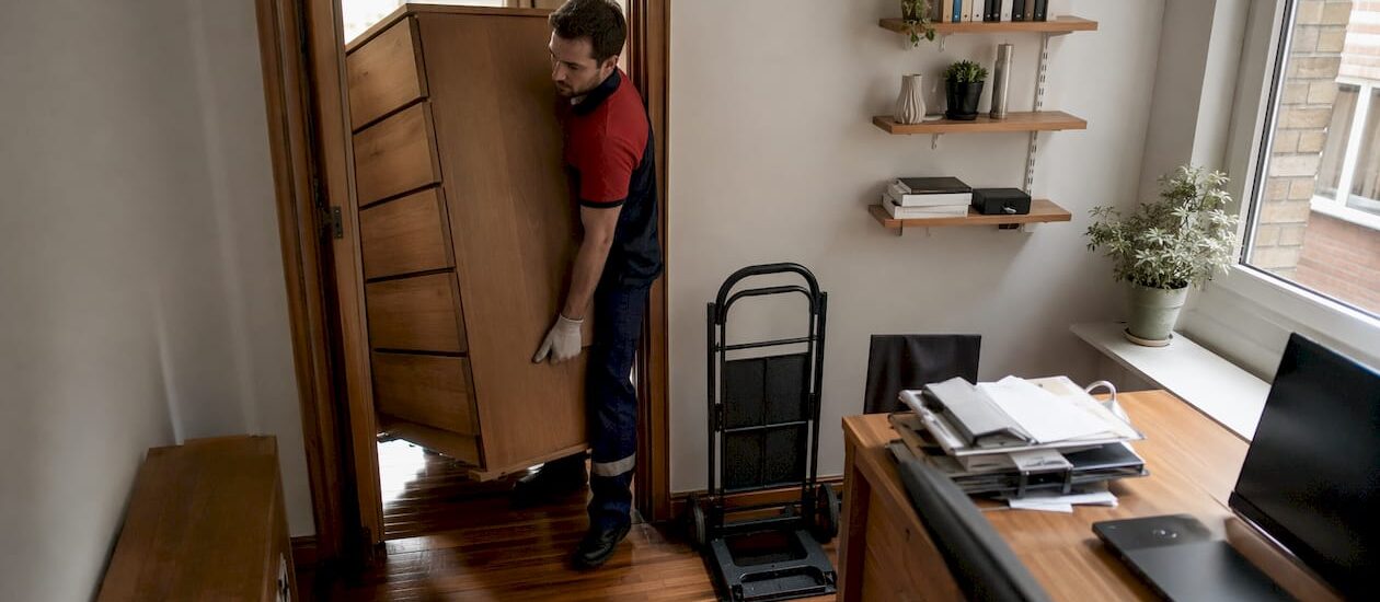 Mover carrying heavy dresser down stairs