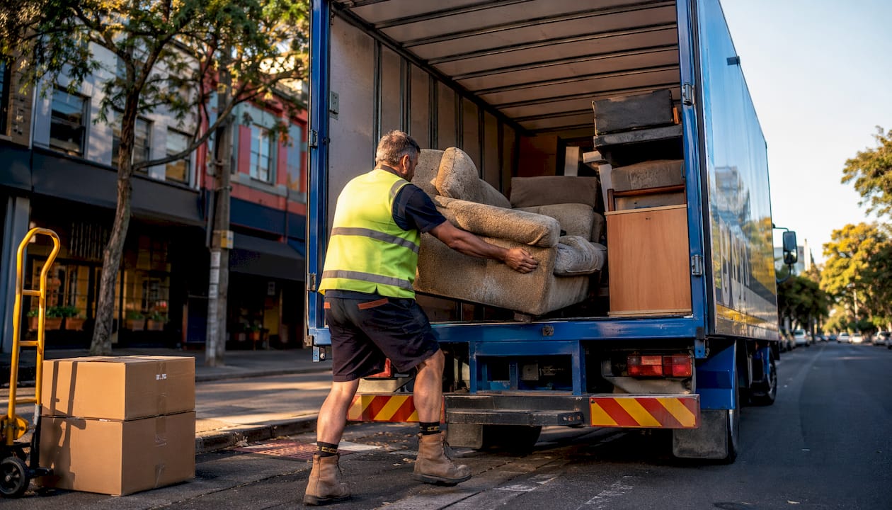 Worker loading sofa into furniture removal truck