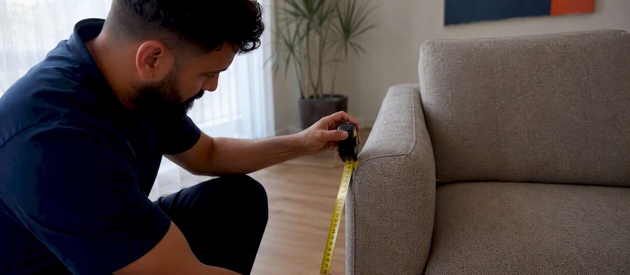 Person measuring sofa near doorway